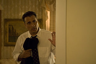man in white dress shirt wearing black necktie holding black textile near wall HD wallpaper